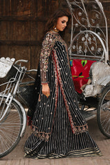 Woman in a black and gold embroidered dress standing next to a vintage carriage.