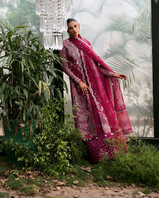 Woman in a pink traditional outfit standing outdoors with greenery around
