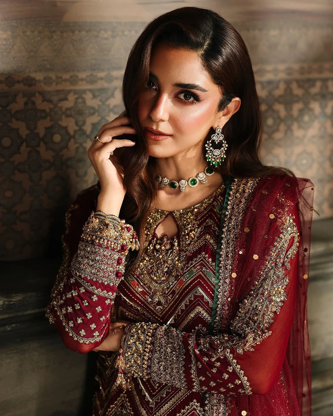 Woman in traditional embroidered outfit with jewelry against a patterned wall