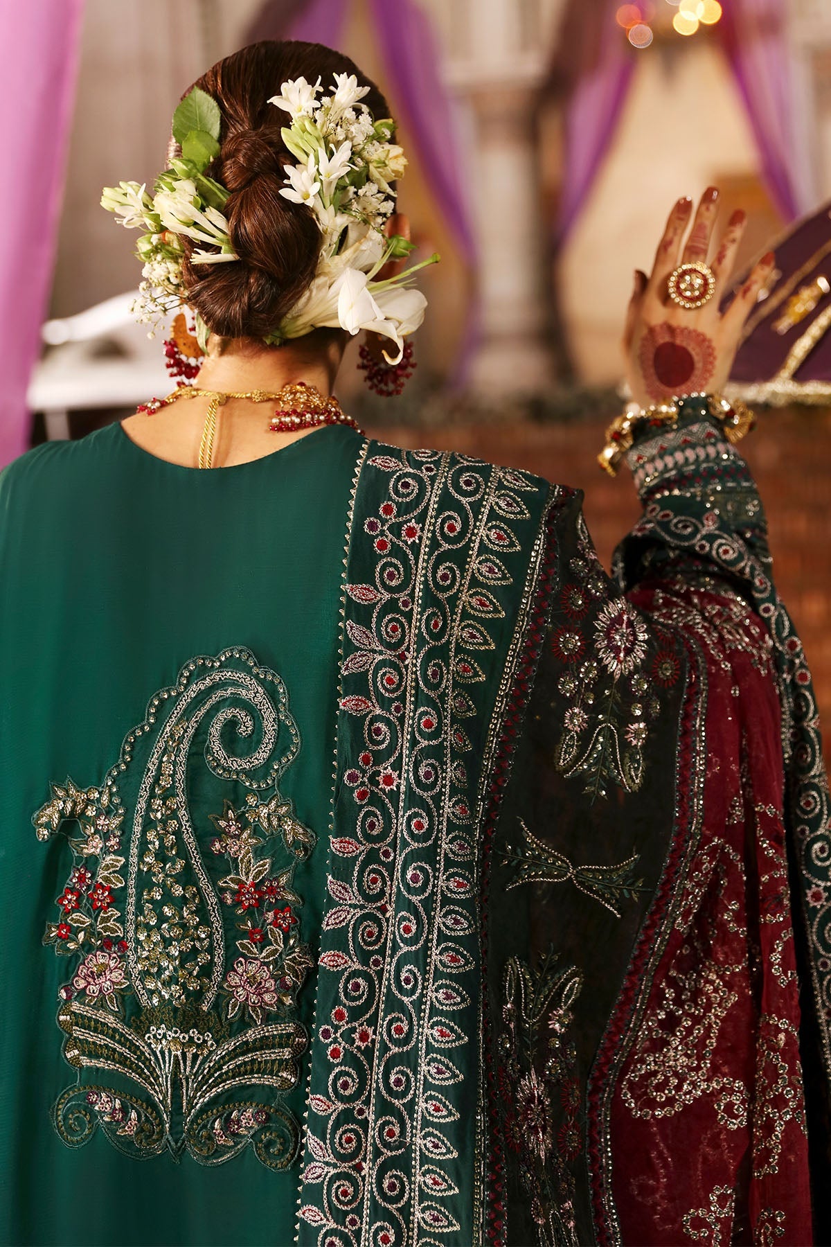 Traditional embroidered garment with intricate patterns and jewelry, set against a blurred decorative background.