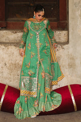 Woman in a green traditional outfit with gold patterns sitting on a red and gold rug.
