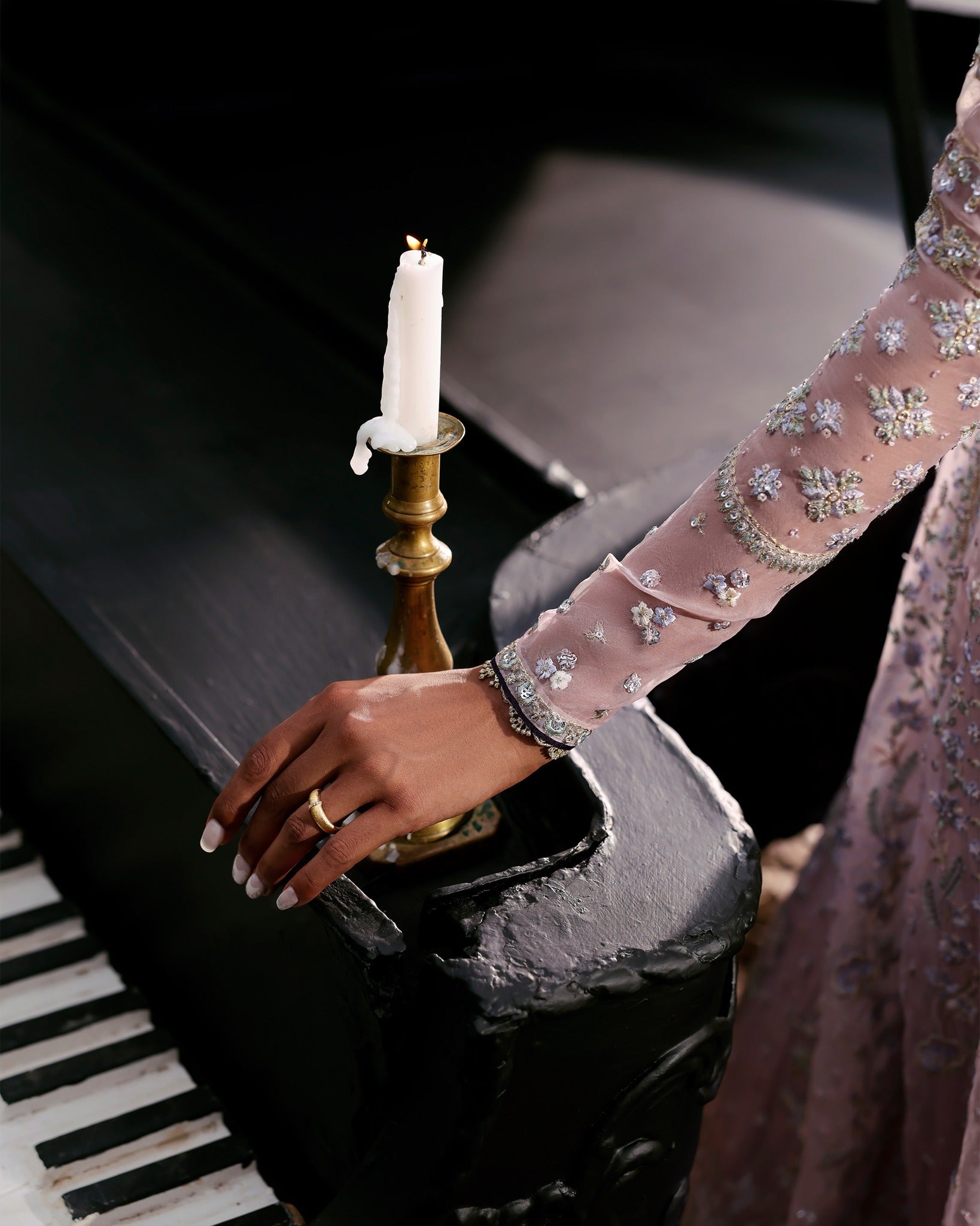 Hand with a ring on a piano next to a candle holder