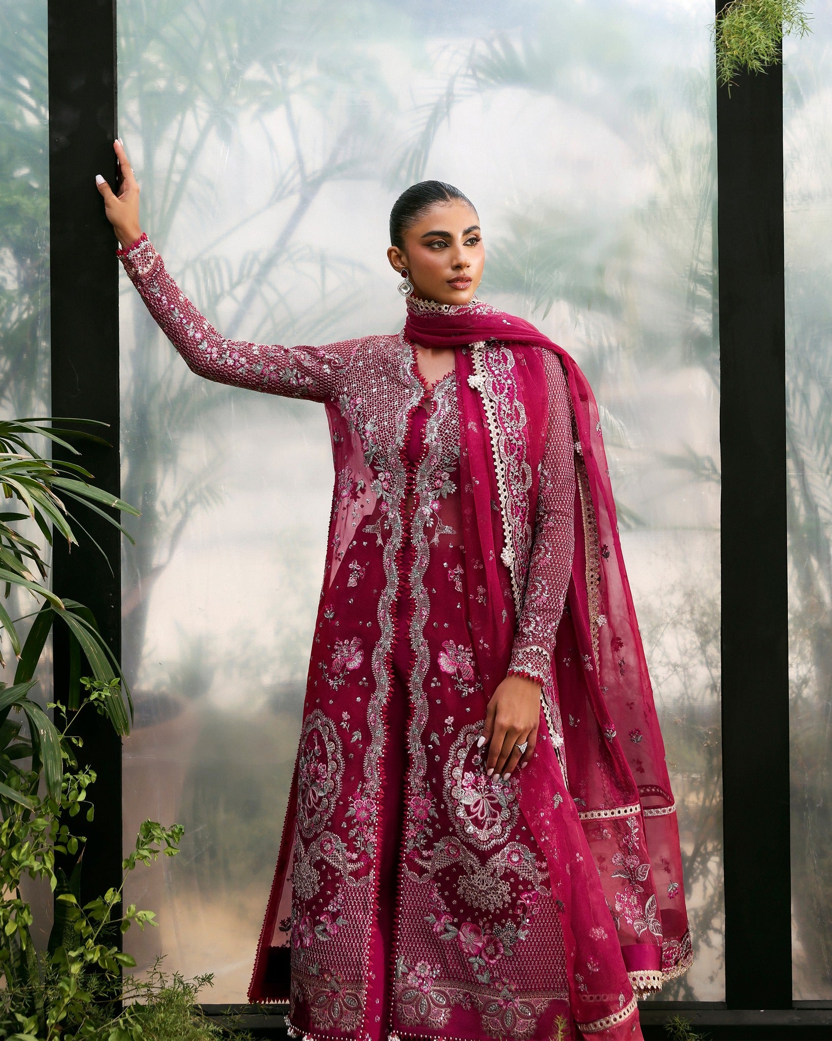 Woman wearing a pink embroidered traditional outfit with a matching dupatta against a natural background.