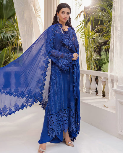 Woman in a blue embroidered outfit standing in a decorative indoor setting with plants.