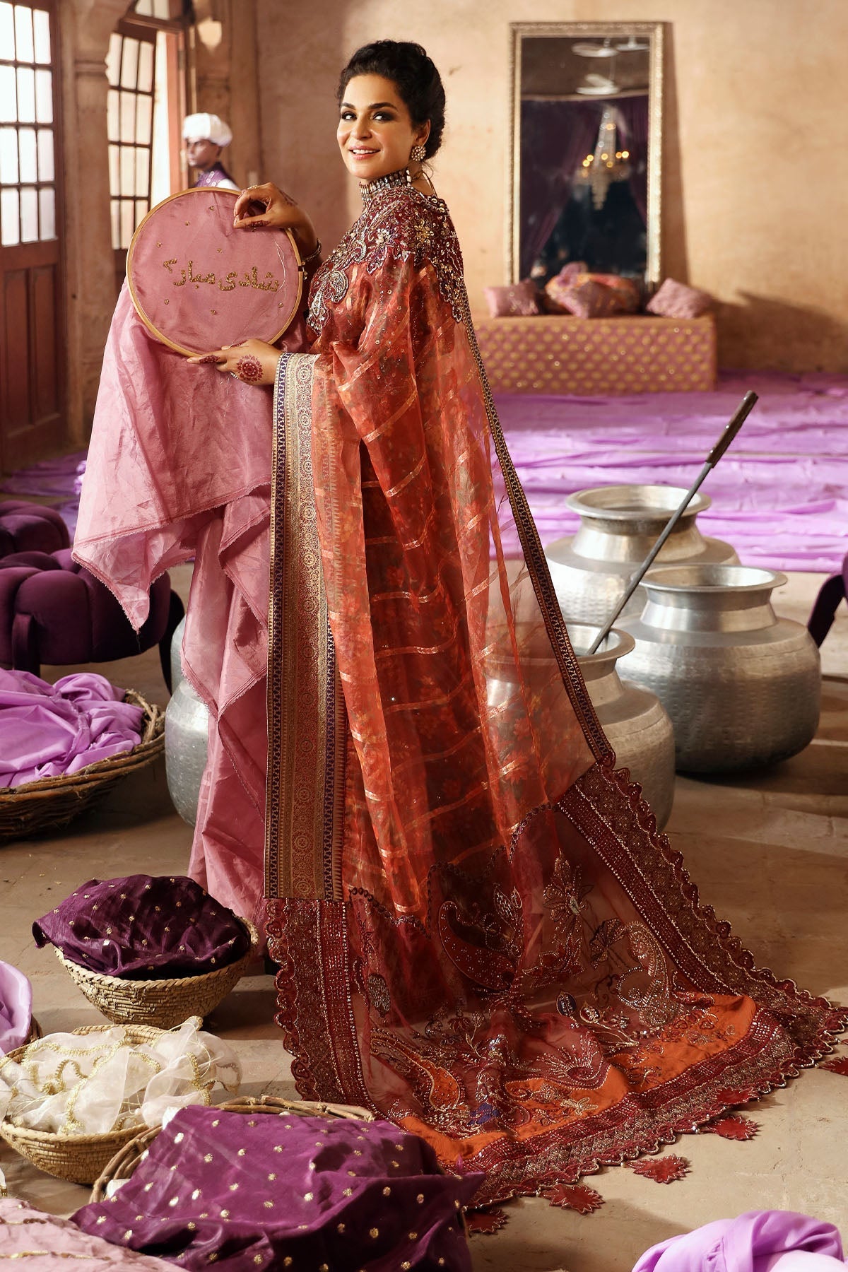 Woman holding a pink fabric with 'Shehla' branding in a traditional setting.