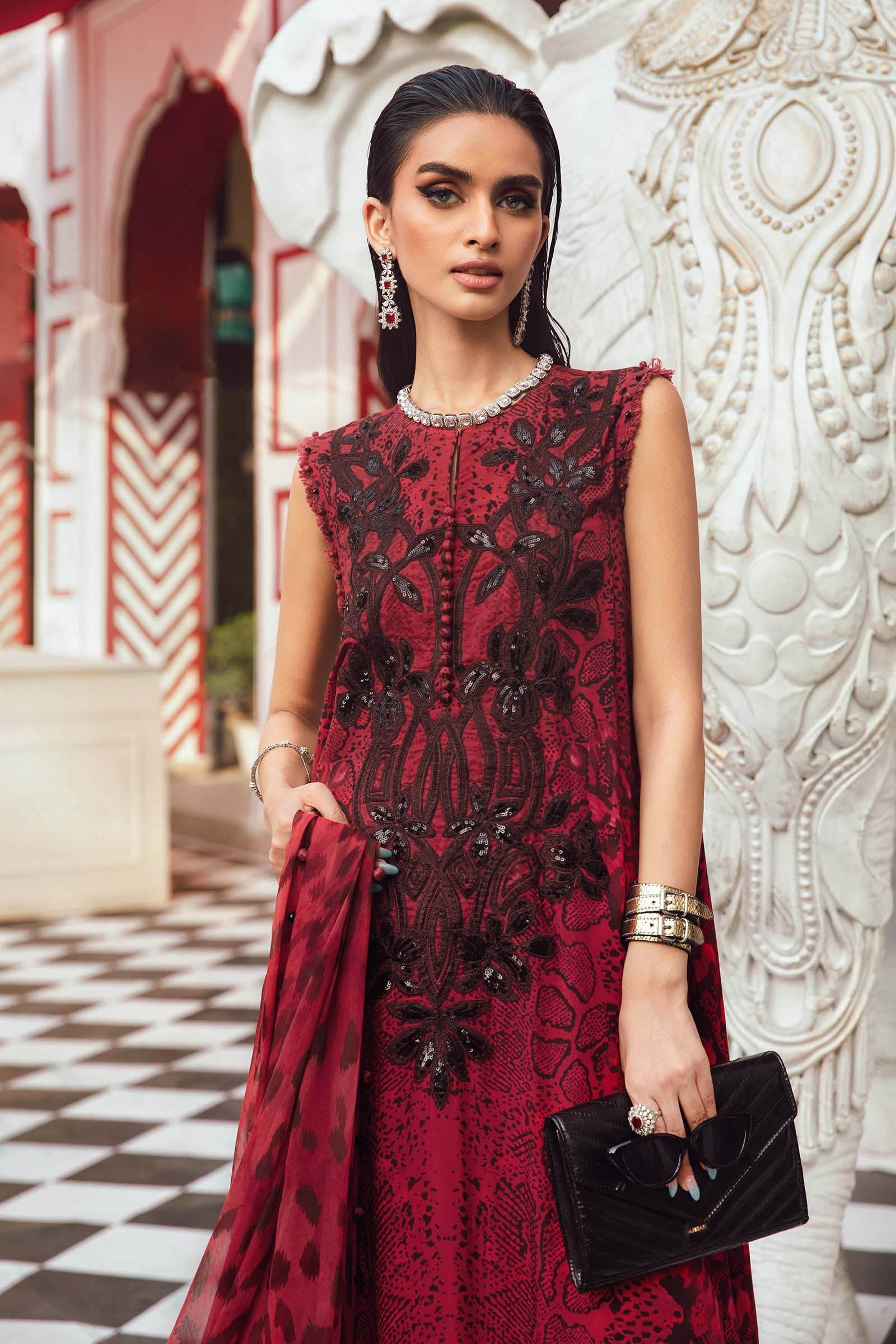 Woman in a red embroidered dress holding a black clutch against an ornate wall.