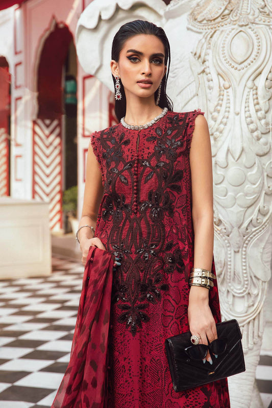 Woman in a red embroidered dress holding a black clutch against an ornate wall.