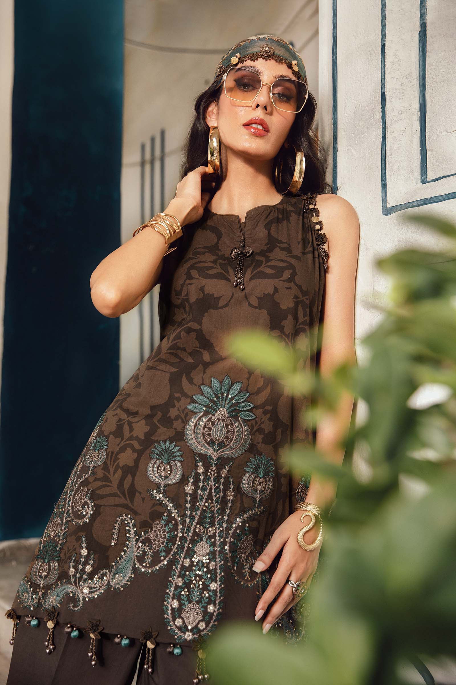Woman wearing a dark brown dress with intricate patterns, standing in a decorative setting.