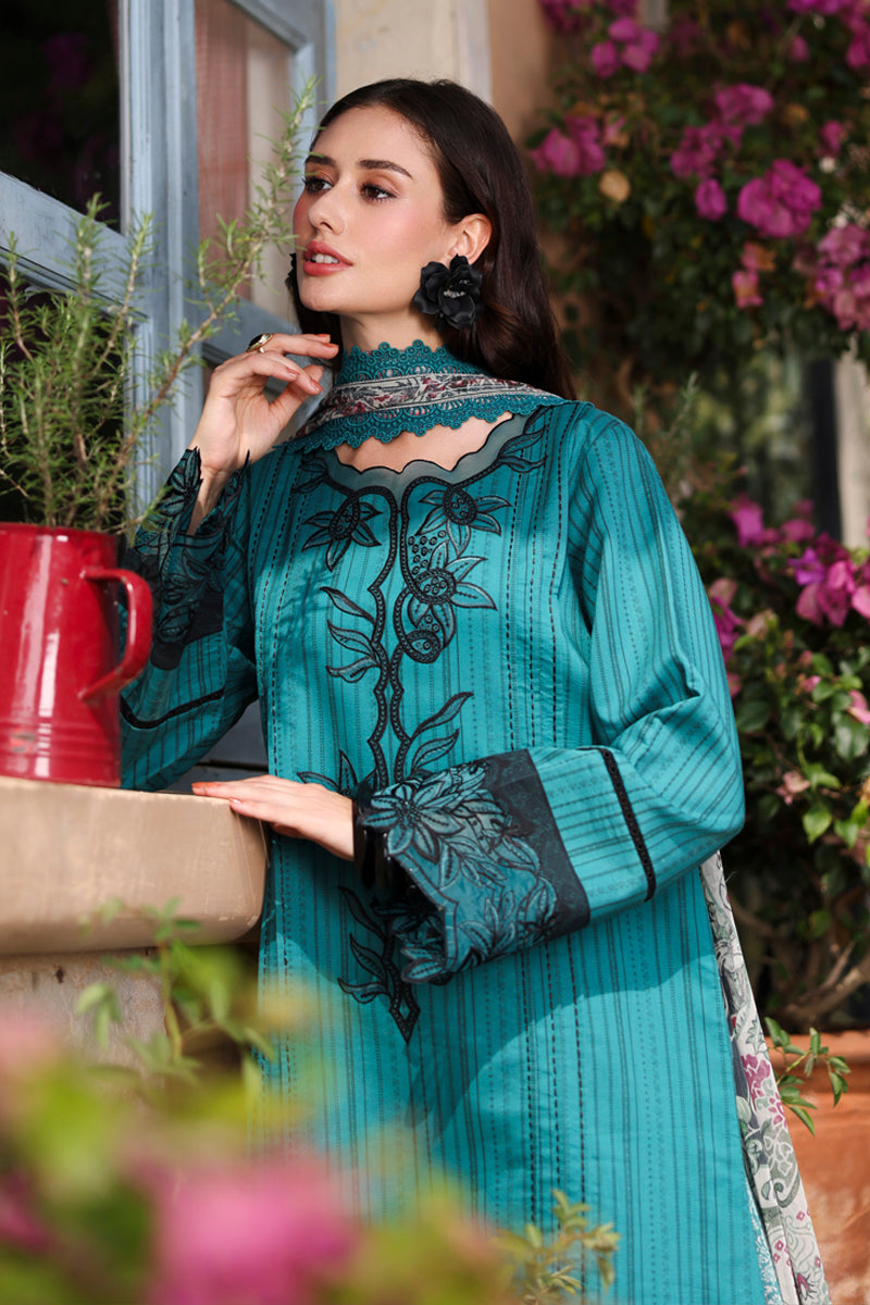 Woman in a teal embroidered outfit standing outdoors with flowers and a red container in the background