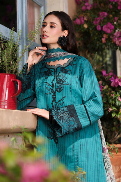Woman in a teal embroidered outfit standing outdoors with flowers and a red container in the background