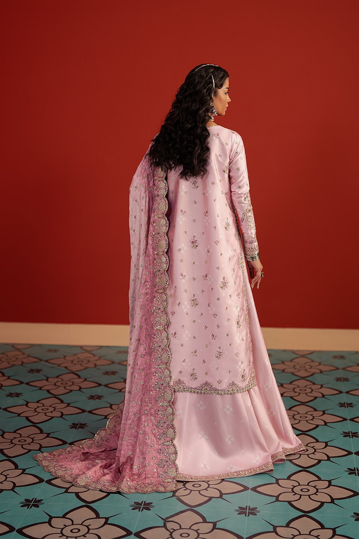Woman in a pink traditional outfit standing against a red wall with a patterned floor.
